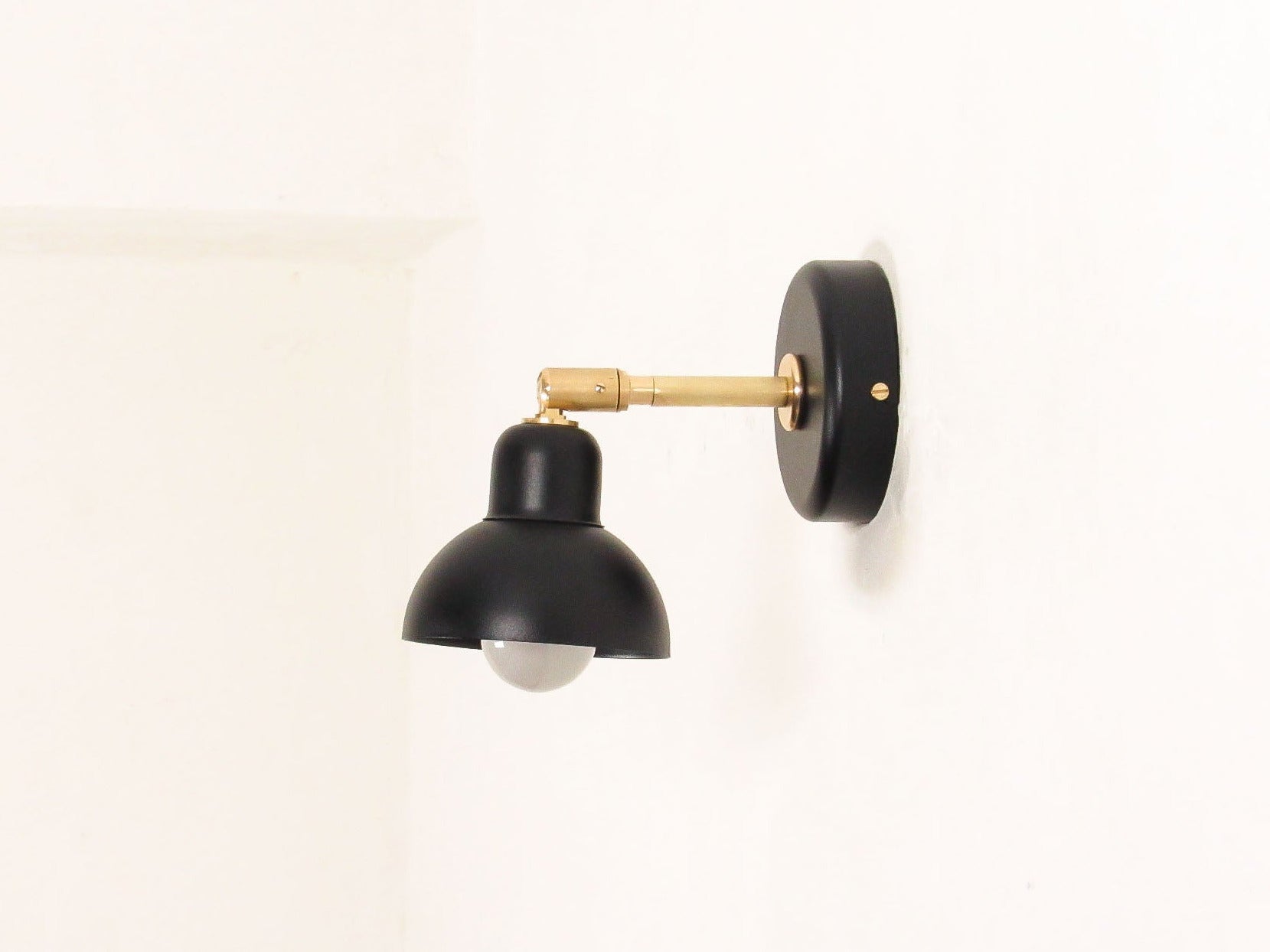Black wall-mounted lamp with brass accent on a white background